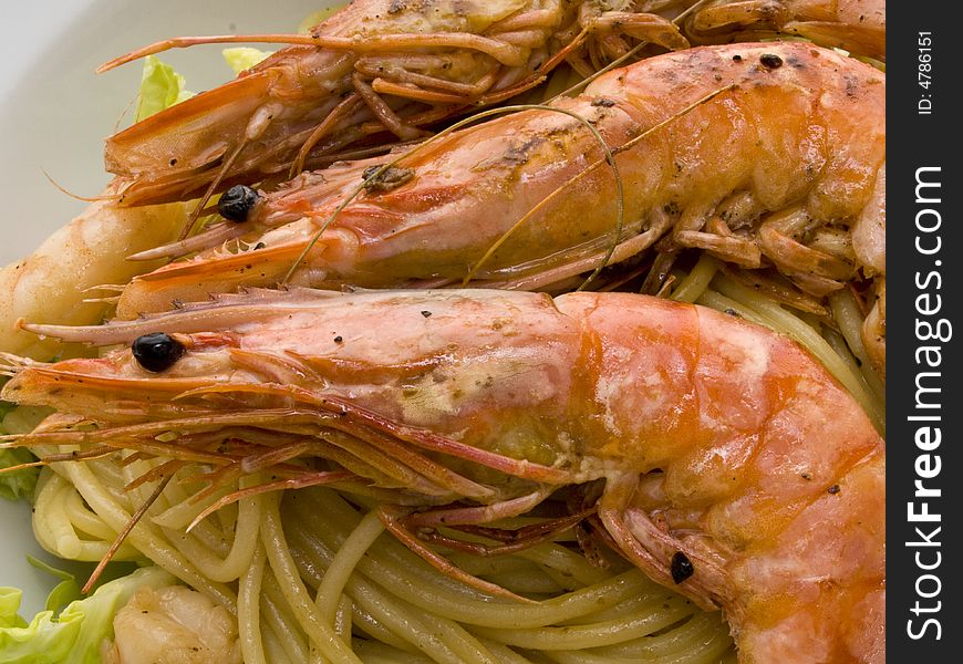 Cooked shrimps on spaghetti with salad on a white plate