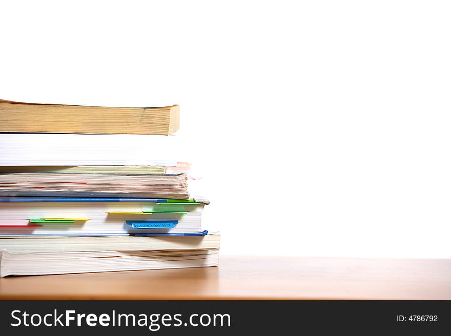 A stack of books sitting on the corner of a desk