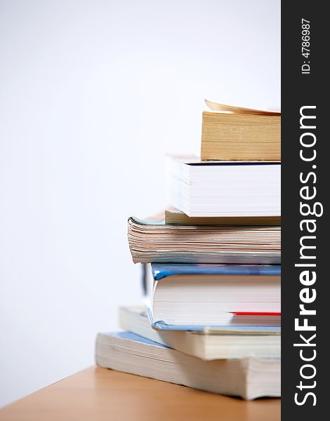 A stack of books sitting on the corner of a desk