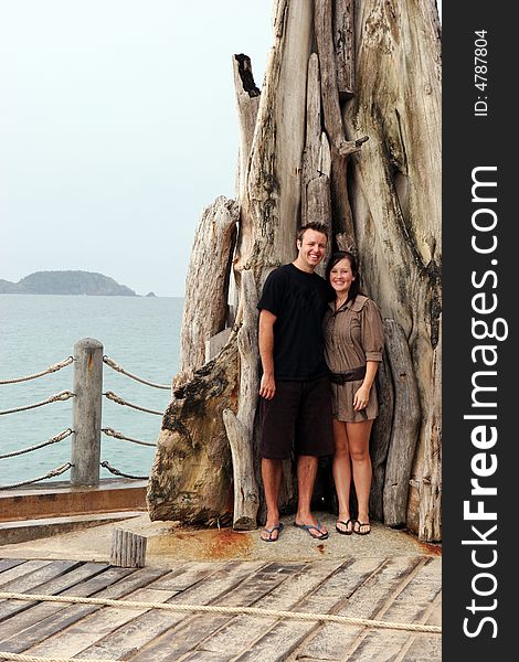 Happy couple standing by a large tree at the beach.