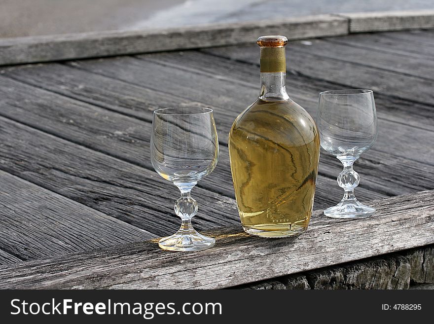 Beautiful vintage yellow bottle of wine and two crystal glasses on the boardwalk. Beautiful vintage yellow bottle of wine and two crystal glasses on the boardwalk