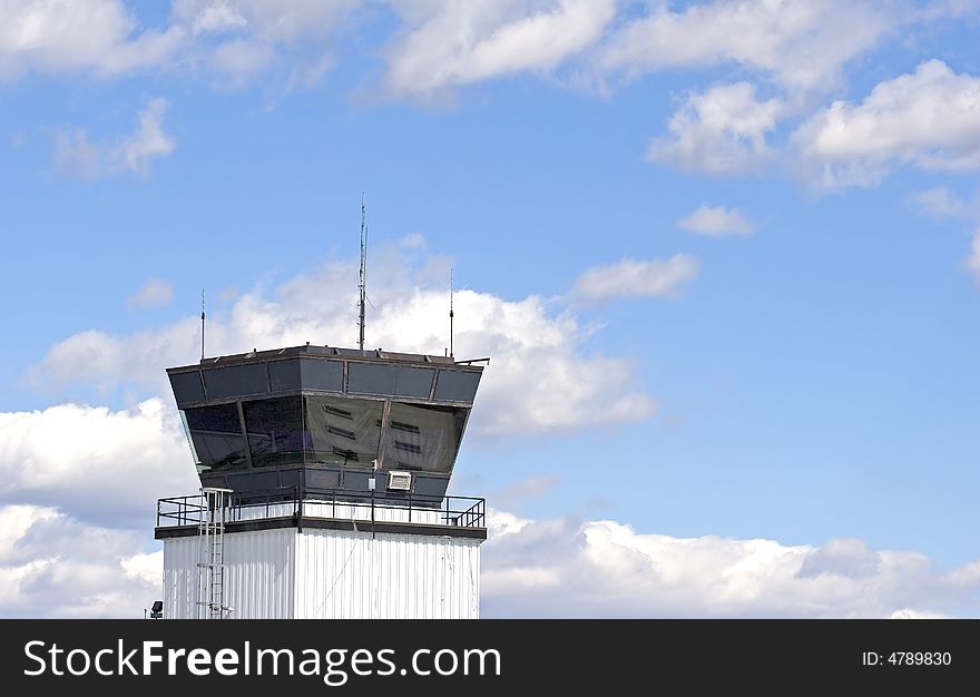 An air traffic control tower at a small regional airport against a blue sky with white puffy clouds. An air traffic control tower at a small regional airport against a blue sky with white puffy clouds