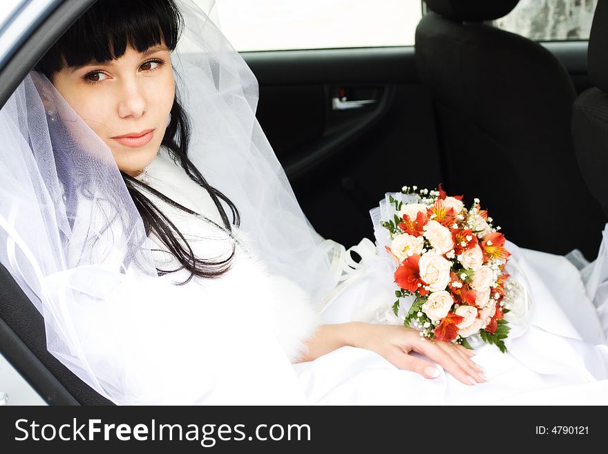 Young bride in wedding wear with bouquet of roses sitting in the car