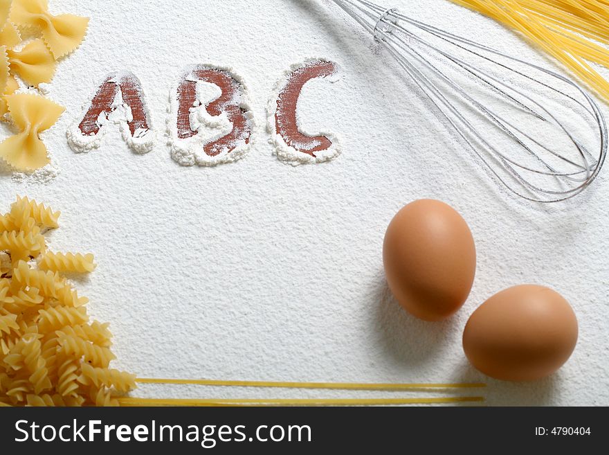 Uncooked macaroni, whisk and eggs on wheat flour, background