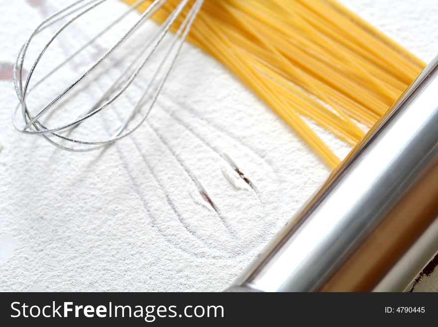 Wire whisk and spaghetti on flour, background