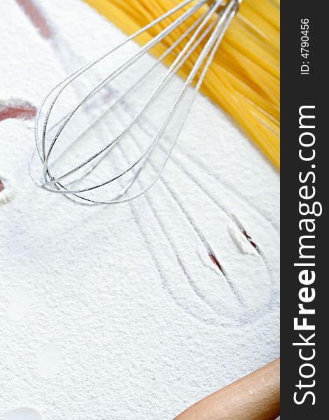 Wire whisk and spaghetti on flour, background