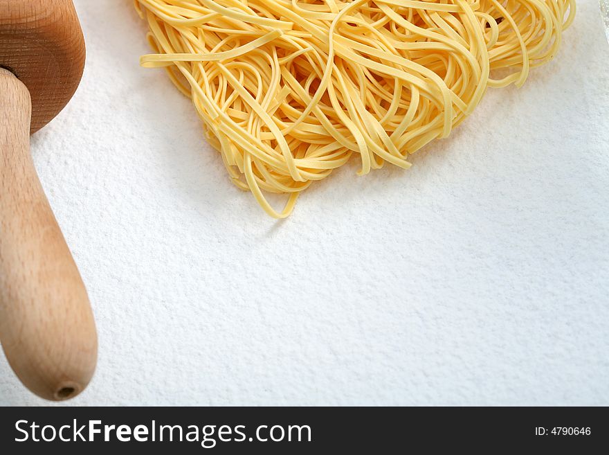 Uncooked noodles and rolling pin on flour, background