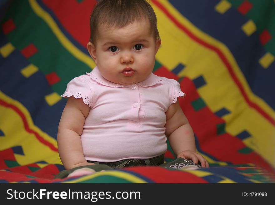 Small baby girl sitting on the colorful bedding. Small baby girl sitting on the colorful bedding