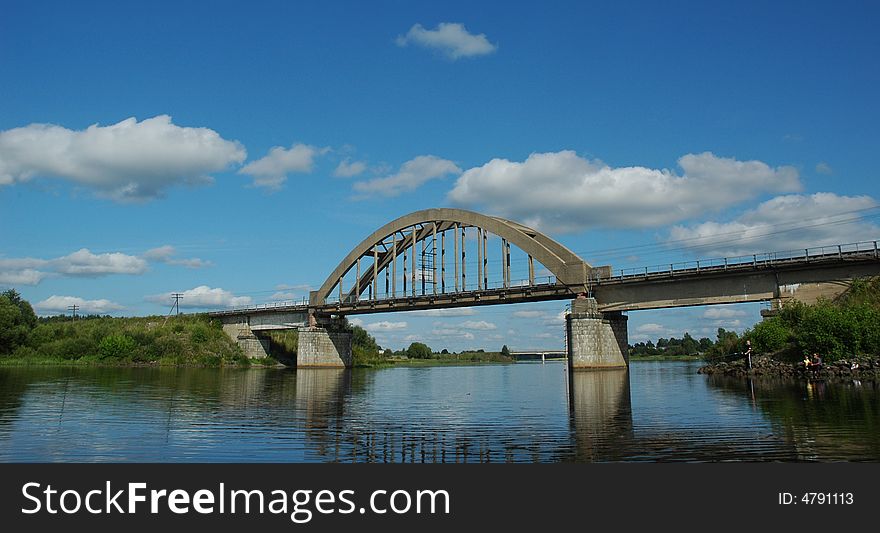 Arch railway bridge over small river with scenic sky.
