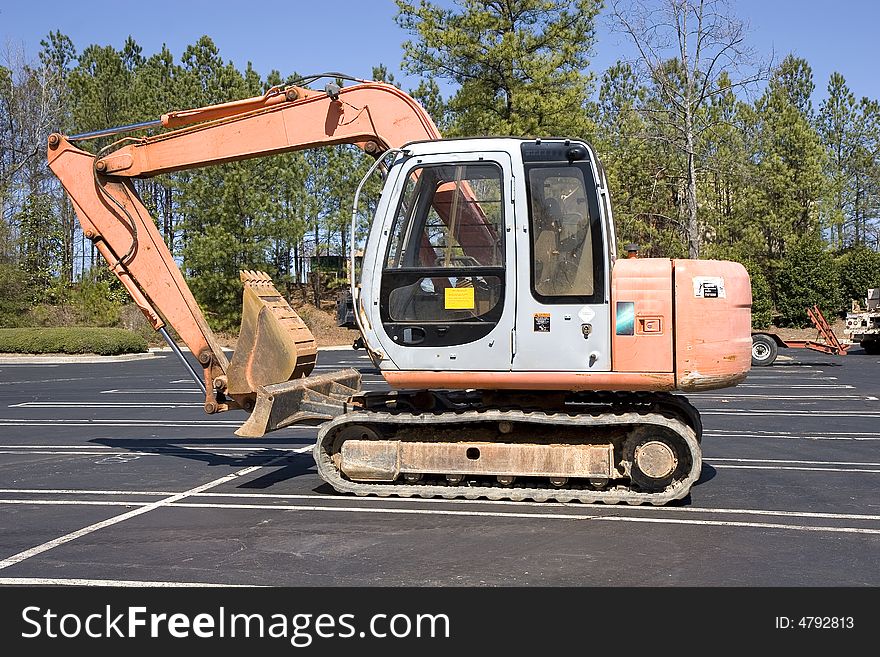 An orange front end loader in a parking lot next to a construction site. An orange front end loader in a parking lot next to a construction site