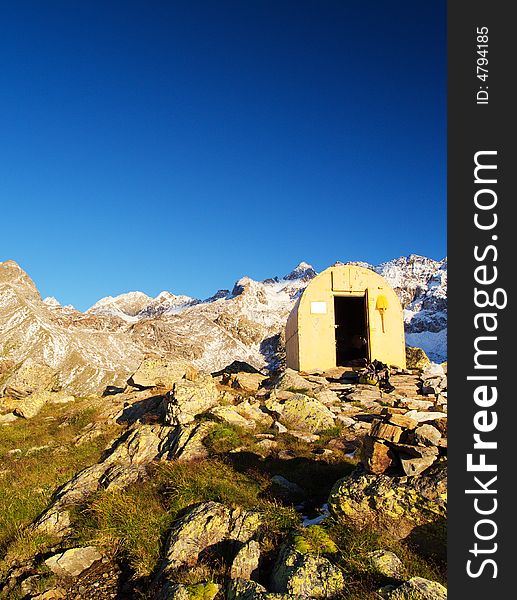 A yellow bivouac in a mountain landscape with a deep blue sky and snow