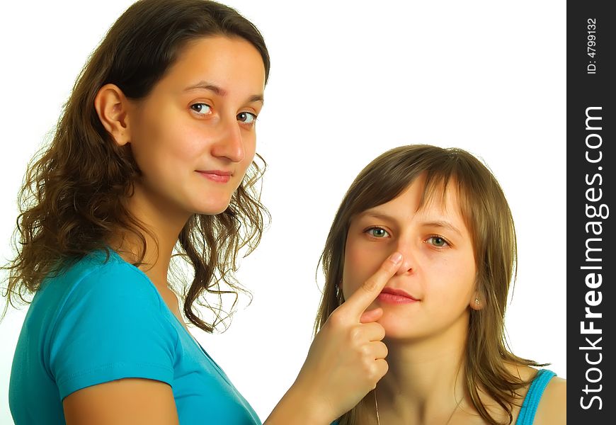 A pretty lady with brown hair puts on her forefinger to an other blond girl's nose. A pretty lady with brown hair puts on her forefinger to an other blond girl's nose