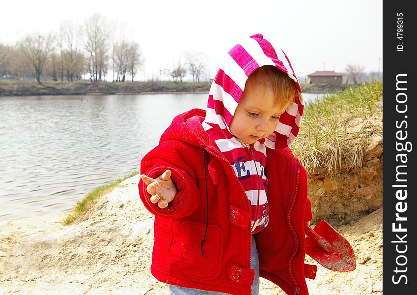 Little girl plays with sand on coast of lake. Little girl plays with sand on coast of lake