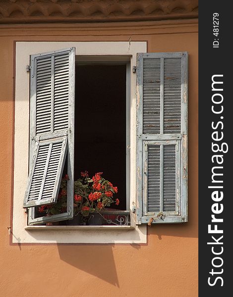 An open shuttered window revealing planted spring flowers on the sill. An open shuttered window revealing planted spring flowers on the sill