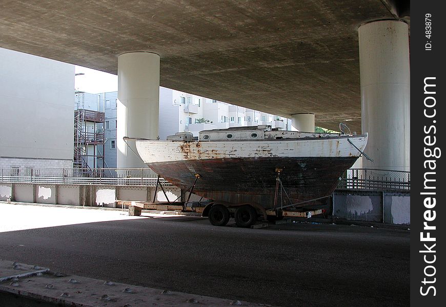 An old sailboat on a trailer under a section of elevated freeway. An old sailboat on a trailer under a section of elevated freeway