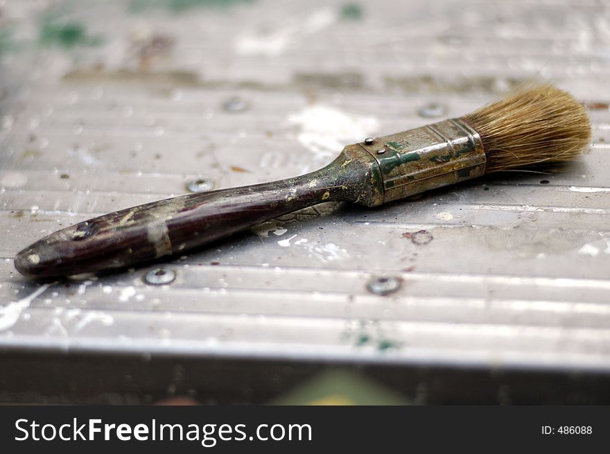 A well used paintbrush on the top step of a metal step ladder