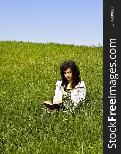 Young woman reading a book in a meadow