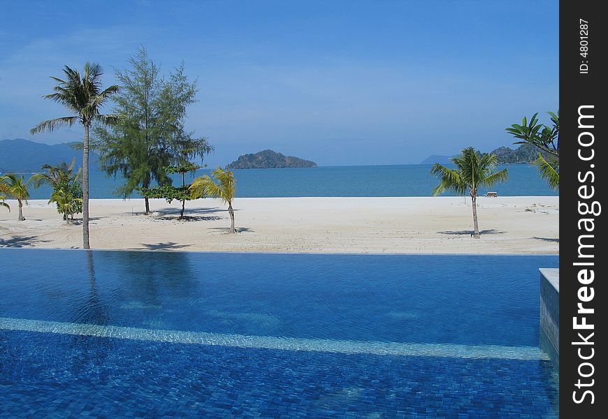 A pool, white beach, blue sea and sky. A pool, white beach, blue sea and sky