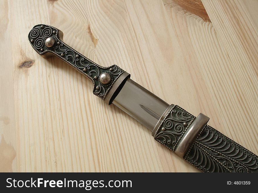 Traditional Georgian steel dagger in pattern stamping sheath on wooden background. Traditional Georgian steel dagger in pattern stamping sheath on wooden background