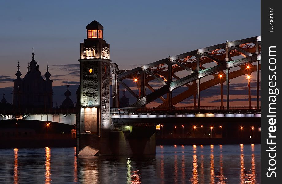 Illuminated bridge across Neva river against the background of the sunset