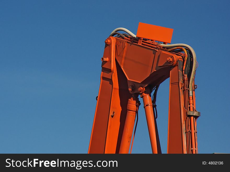 Orange backhoe construction equipment against blue sky. Orange backhoe construction equipment against blue sky