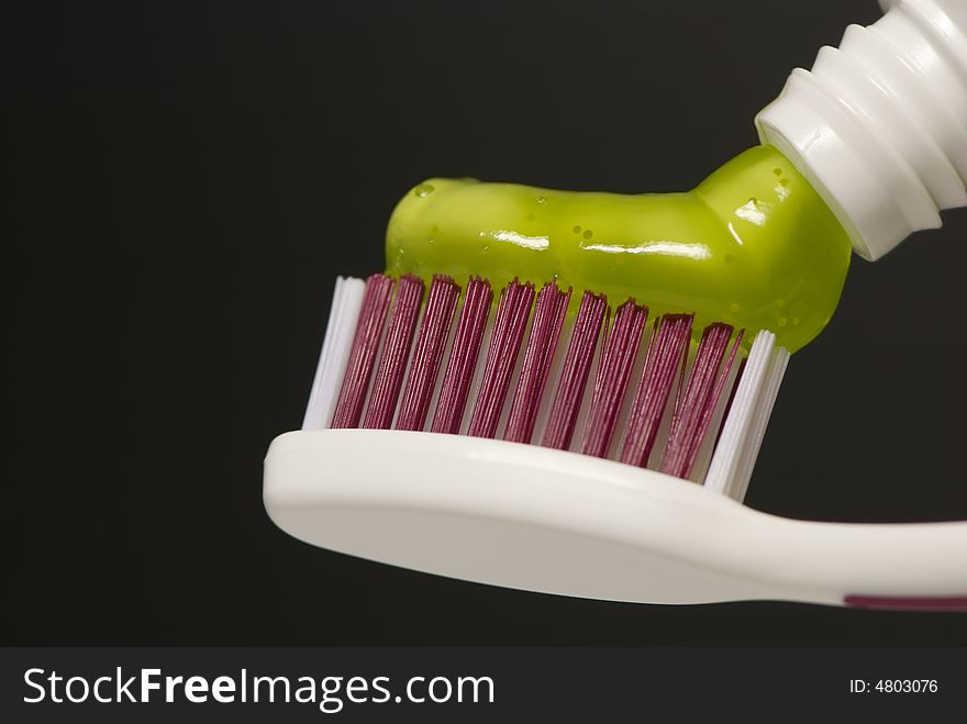 Green toothpaste on toothbrush against dark background
