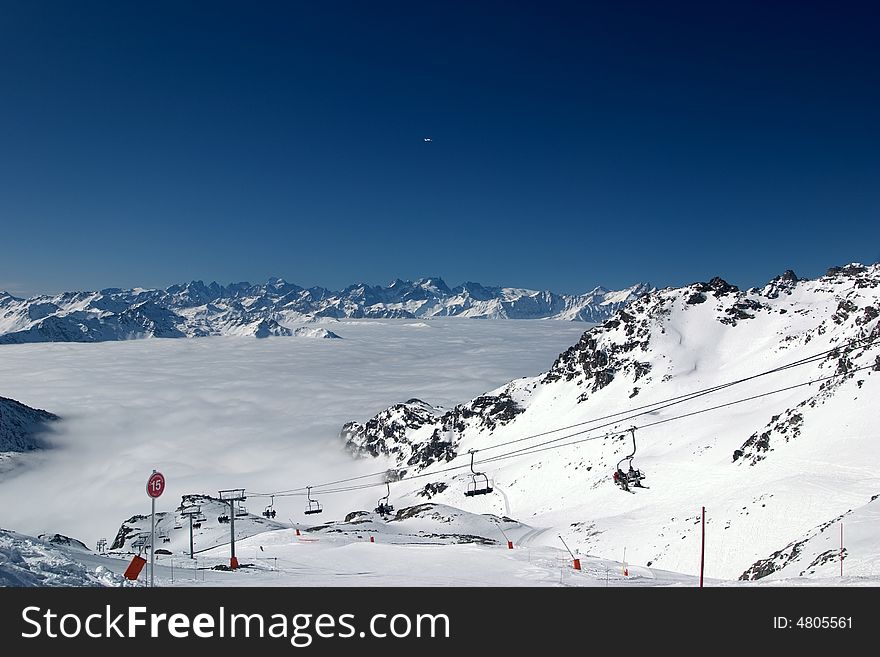 A ski lift and a ski slope sign, above the clouds