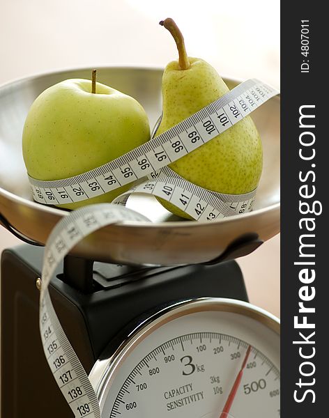 Apple and pear on kitchen scales with tape measure. Apple and pear on kitchen scales with tape measure