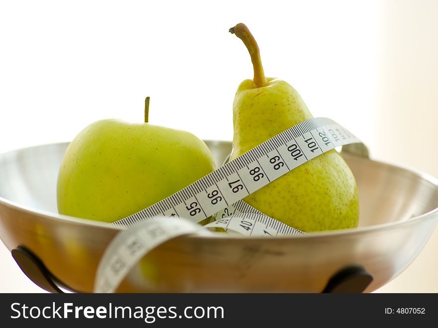 Apple and pear on kitchen scales with tape measure. Apple and pear on kitchen scales with tape measure