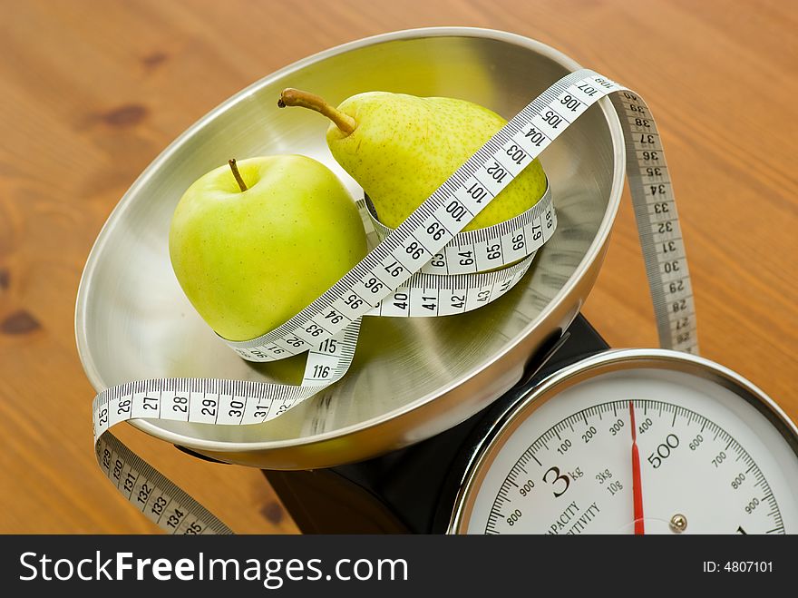 Apple and pear on kitchen scales with tape measure. Apple and pear on kitchen scales with tape measure