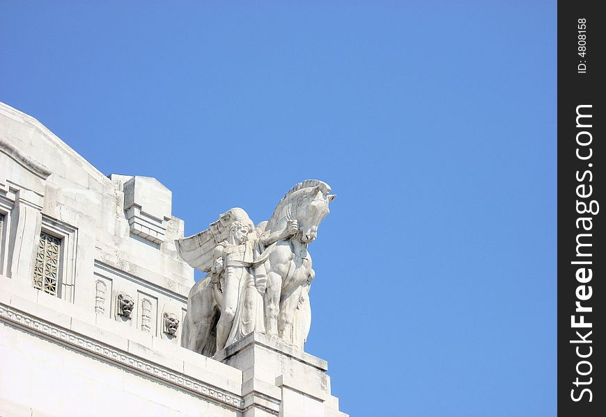 A statue of the train station of Milan, under a blue sky. A statue of the train station of Milan, under a blue sky