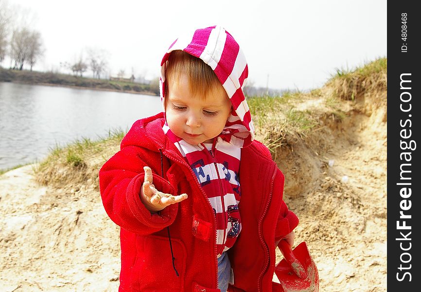 Little girl plays with sand on coast of lake. Little girl plays with sand on coast of lake