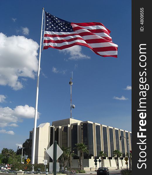 A flag stands tall, way above the ground and is towering over a building. A flag stands tall, way above the ground and is towering over a building