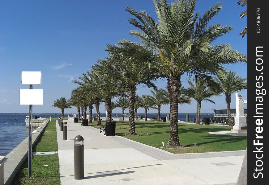 A park with straight rows of palm trees, benches, trash cans, a well manicured lawn and concrete slab overlooks the ocean. A park with straight rows of palm trees, benches, trash cans, a well manicured lawn and concrete slab overlooks the ocean.