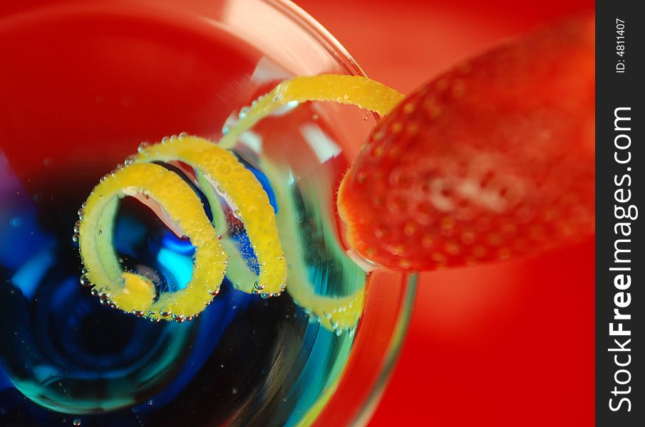 Cocktail with blue curacao, strawberry and lemon paring in wineglass. red, yellow and blue colours. Cocktail with blue curacao, strawberry and lemon paring in wineglass. red, yellow and blue colours