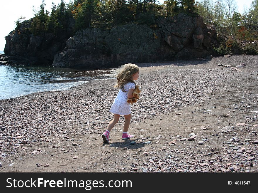 A long shot of a little girl holding her stuffed toy, along a rocky shoreline. A long shot of a little girl holding her stuffed toy, along a rocky shoreline.