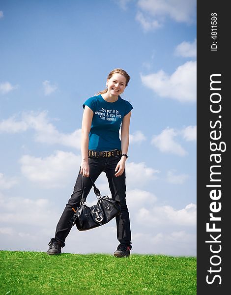 The young attractive girl with a handbag on a background of the blue sky