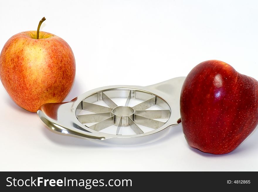 A view of two delicious red apples next to a handy, stainless steel apple slicer on a white background. A view of two delicious red apples next to a handy, stainless steel apple slicer on a white background.