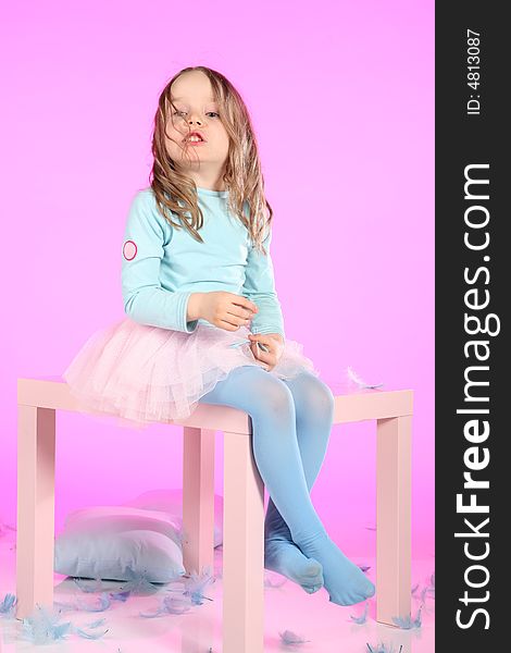 Five years old girl having fun with blue pillows and feathers at small table on pink colored background. Studio hi-res shot. Five years old girl having fun with blue pillows and feathers at small table on pink colored background. Studio hi-res shot.