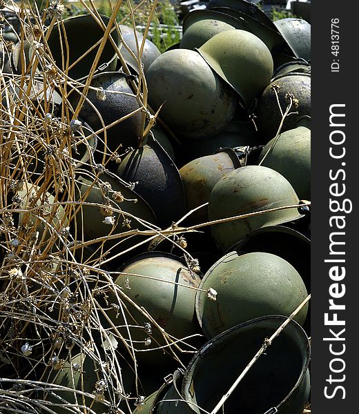 Abandoned Army helmets stacked up in the weeds. Abandoned Army helmets stacked up in the weeds