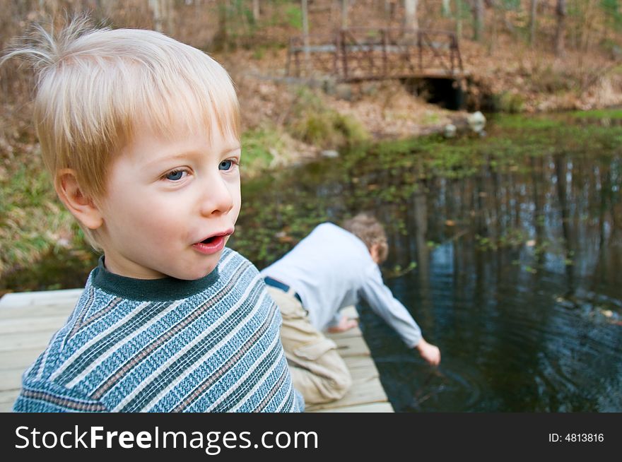 Two boys play on a dock by a scenic pond. Two boys play on a dock by a scenic pond