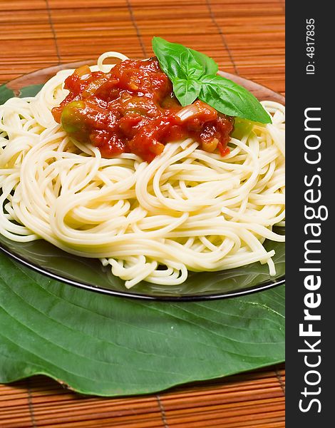 Italian dinner: spaghetti. Macaroni with tomato sauce with garlic, olives and fresh basil isolated on green leaf.