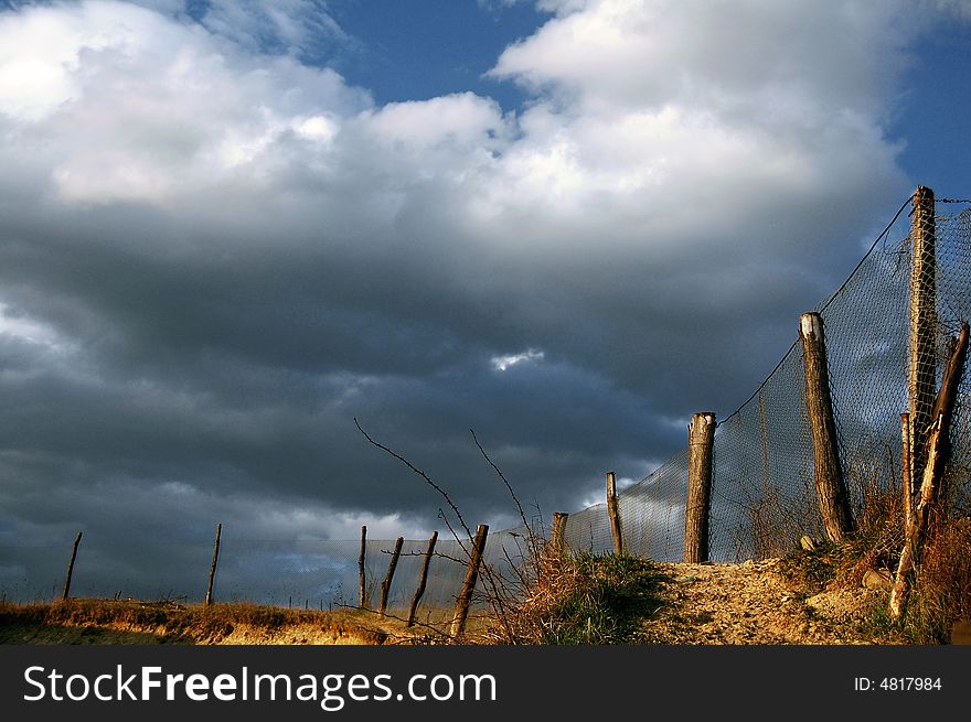 A tawny net fence with pillars and a cloudy sky. A tawny net fence with pillars and a cloudy sky