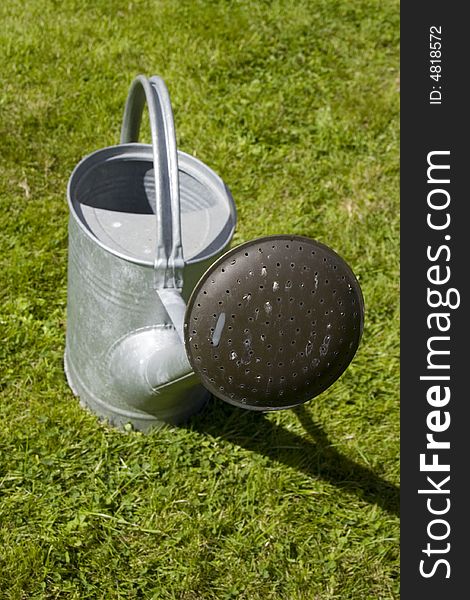 A tin watering can on a grass lawn. A tin watering can on a grass lawn