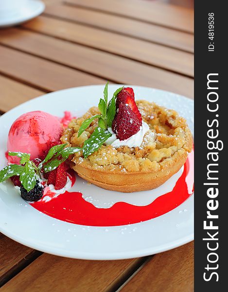 Freshly baked apple crumble pie with various berries, mint leaf and strawberry ice cream on a white plate.