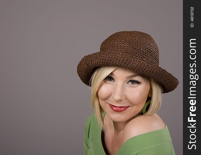 A blonde in a green blouse and a silly brown hat with a small smile. A blonde in a green blouse and a silly brown hat with a small smile