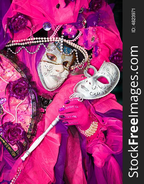 Person holding a silver mask wearing a pink costume at the Venice Carnival. Person holding a silver mask wearing a pink costume at the Venice Carnival