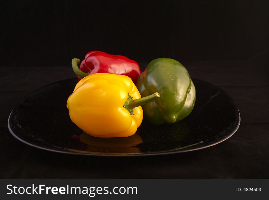 Three Peppers on Black in the Plate (Red, Green, Yellow). Three Peppers on Black in the Plate (Red, Green, Yellow)