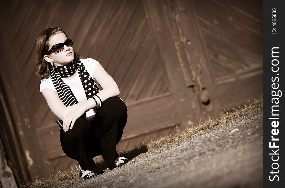 Portrait of a squatting tween girl in front of old double doors.  In sepia tone. Portrait of a squatting tween girl in front of old double doors.  In sepia tone.