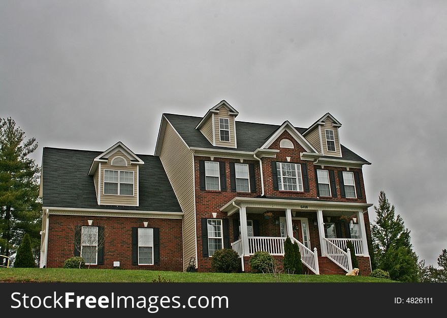 Large three story brick home with dormer windows and a landscaped yard.